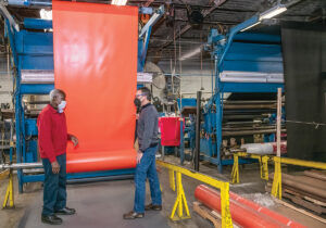 OVERCOMING OBSTACLES: Daniel Dwight, right, CEO and president of Pawtucket membrane manufacturer Cooley Group, goes over the company’s oil boom containment technology with Larry Akinlapa, fabric inspector. The company has seen record growth despite being hamstrung by labor shortages and supply chain bottlenecks. / PBN PHOTO/MICHAEL SALERNO