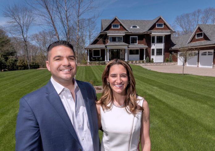 FORM AND FUNCTION: Jennifer and Gary Mello, owners of Seekonk-based The Mello Group, are seen in front of a home that Gary Mello designed. The 4,000-square-foot home has a large, open living area, a 12-foot island in the kitchen and a two-sided, two-story chimney with a fireplace both inside and out. / PBN PHOTO/MICHAEL SALERNO FORM AND FUNCTION: Jennifer and Gary Mello, owners of Seekonk-based The Mello Group, are seen in front of a home that Gary Mello designed. The 4,000-square-foot home has a large, open living area, a 12-foot island in the kitchen and a two-sided, two-story chimney with a fireplace both inside and out. / PBN PHOTO/MICHAEL SALERNO