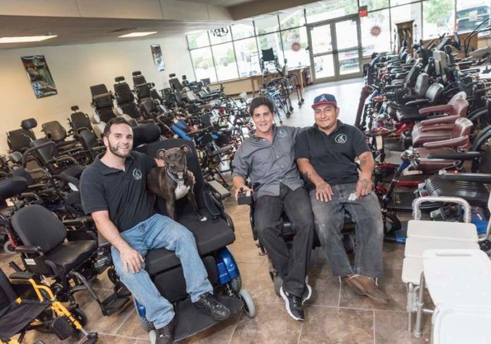 ON A GOOD ROLL: Mobility Equipment Recyclers accepts donations of new and used mobility medical devices and equipment, including powered wheelchairs, for resale at a discount. From left are Andrew Celani, store manager, Bailey, company mascot, John Perrotti, owner and Raymond Perez, technician. / PBN PHOTO/MICHAEL SALERNO ON A GOOD ROLL: Mobility Equipment Recyclers accepts donations of new and used mobility medical devices and equipment, including powered wheelchairs, for resale at a discount. From left are Andrew Celani, store manager, Bailey, company mascot, John Perrotti, owner and Raymond Perez, technician. / PBN PHOTO/MICHAEL SALERNO