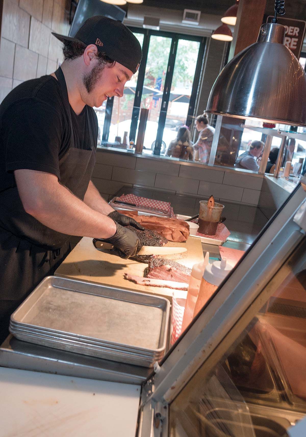 SLOW-COOKED: Sous-chef Nate Brothers cuts a freshly smoked brisket for customers at Durk’s Bar-B-Q, a new restaurant serving slow-cooked meat, such as brisket and pork belly, in Providence. / PBN PHOTO/ MICHAEL SALERNO