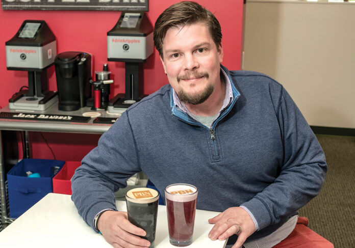 WRITTEN IN FROTH: Jeb Barnes, head of sales and operations at Ripples U.S. in North Kingstown, displays a beverage with a custom-made design in the foam, made by a Ripple Maker machine behind him.
/ PBN PHOTO/MICHAEL SALERNO WRITTEN IN FROTH: Jeb Barnes, head of sales and operations at Ripples U.S. in North Kingstown, displays a beverage with a custom-made design in the foam, made by a Ripple Maker machine behind him.
/ PBN PHOTO/MICHAEL SALERNO