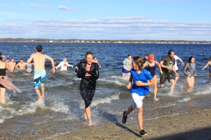 PARTICIPANTS EMERGE FROM the water at Goddard Memorial State Park Beach in Warwick on Jan. 1 during the ninth annual Laid-back Fitness Frozen Clam Dip & Obstaplunge. The event raised $14,177 to support Mentor Rhode Island. / COURTESY LAID-BACK FITNESS