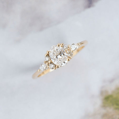 A 14k gold ring featuring an oval center stone with smaller round and pear side stones.