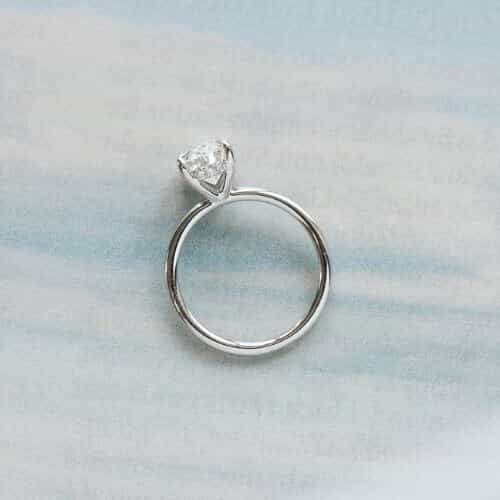 An oval, 14k white gold solitaire featuring a hidden halo of small round diamonds between the claws.