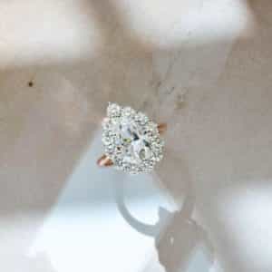 A 14k white and rose gold ring with a pear moissanite center stone and 3mm moissanites on a halo.