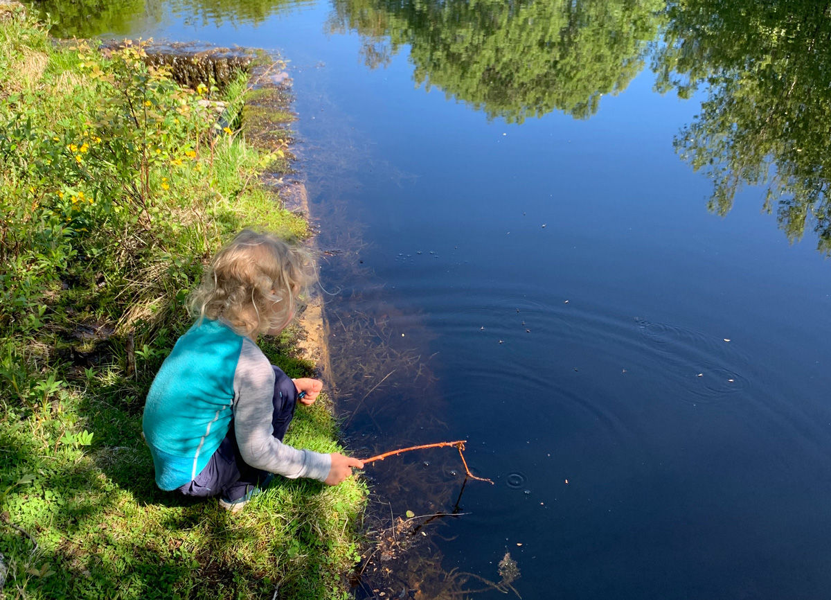 Gutt leker med pinne i vannet