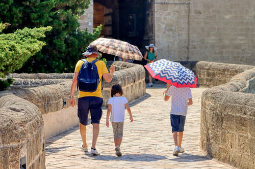 Vater schützt seine Kinder mit Regenschirmen vor der Sonne an einem sehr heißen Tag.