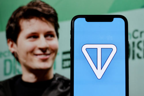 In dieser Fotoabbildung wird das Logo des Toncoin-Tokens auf einem Smartphone mit CEO Pavel Durov im Hintergrund angezeigt.