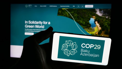 Person hält Smartphone mit Logo der UN-Klimakonferenz 2024 COP29 vor der Website. 