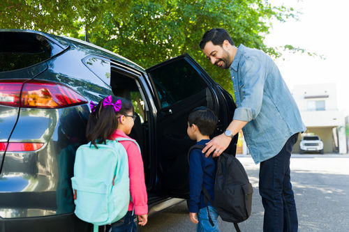 Vater fährt Kind / Kinder mit dem Auto zur Schule.