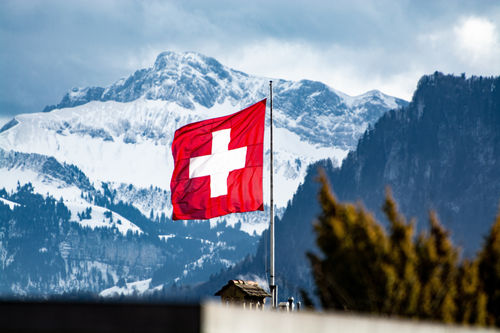 Helle rote Schweizer Flagge im Wind mit Schweizer Bergen auf dem Hintergrund