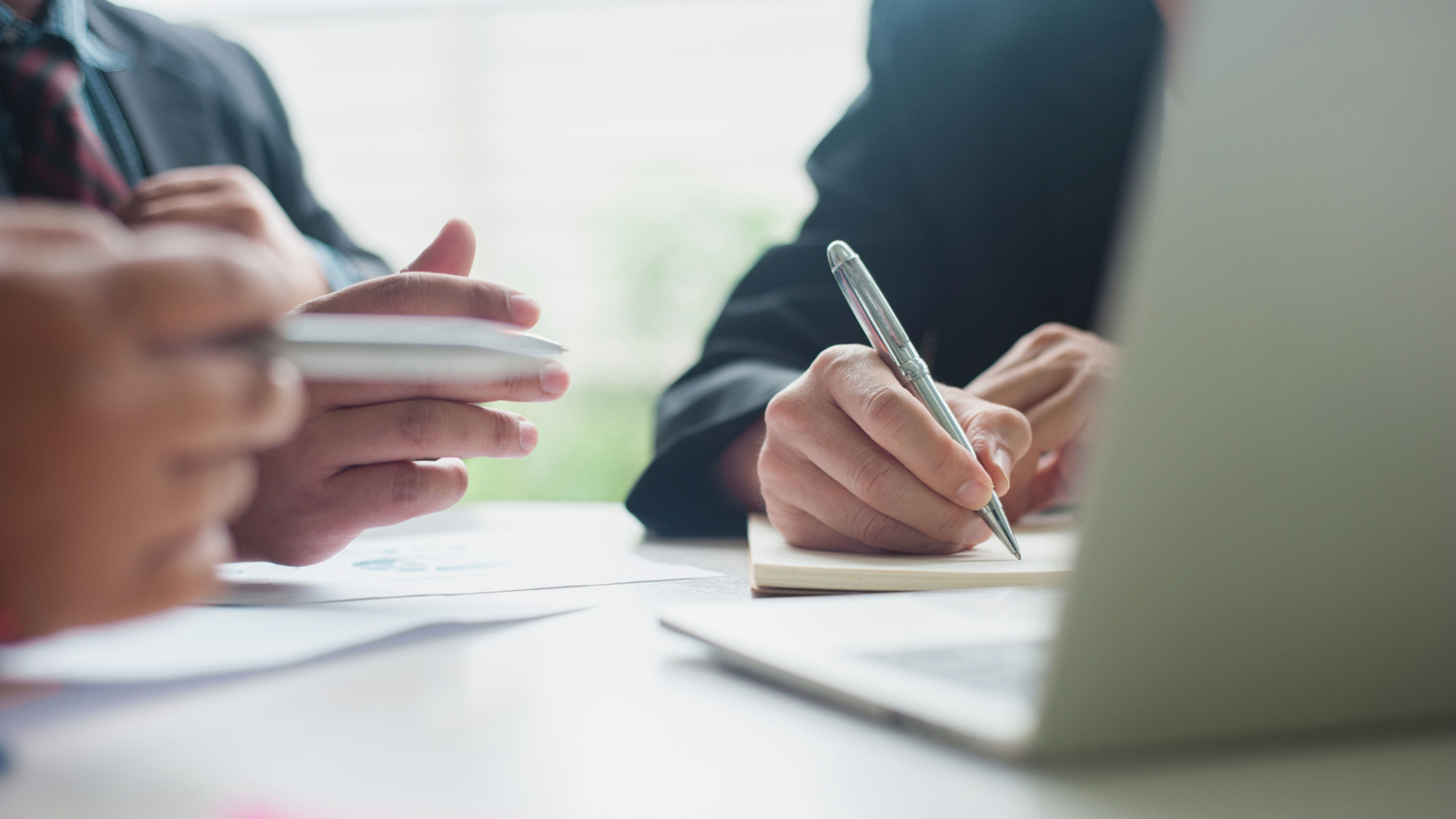 Two people in a meeting, writing down notes