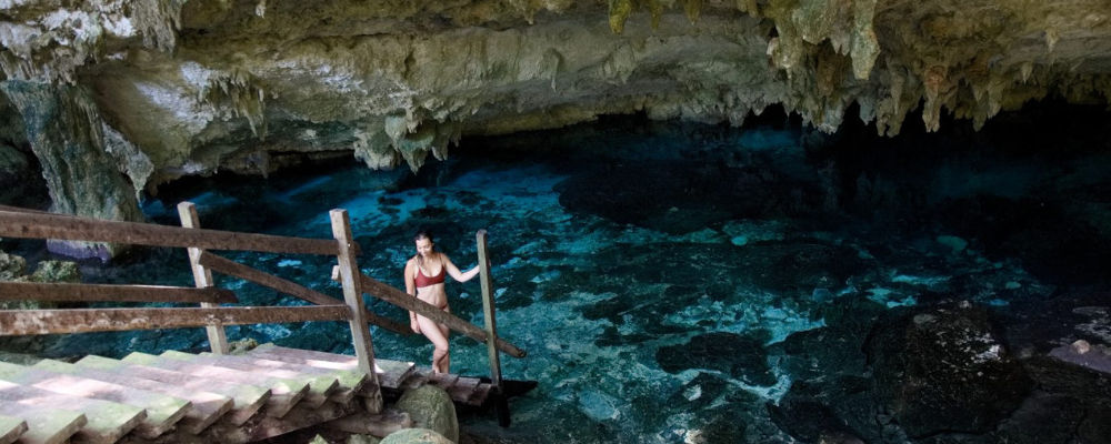 Mujer en entrada a cenote subterráneo con escaleras