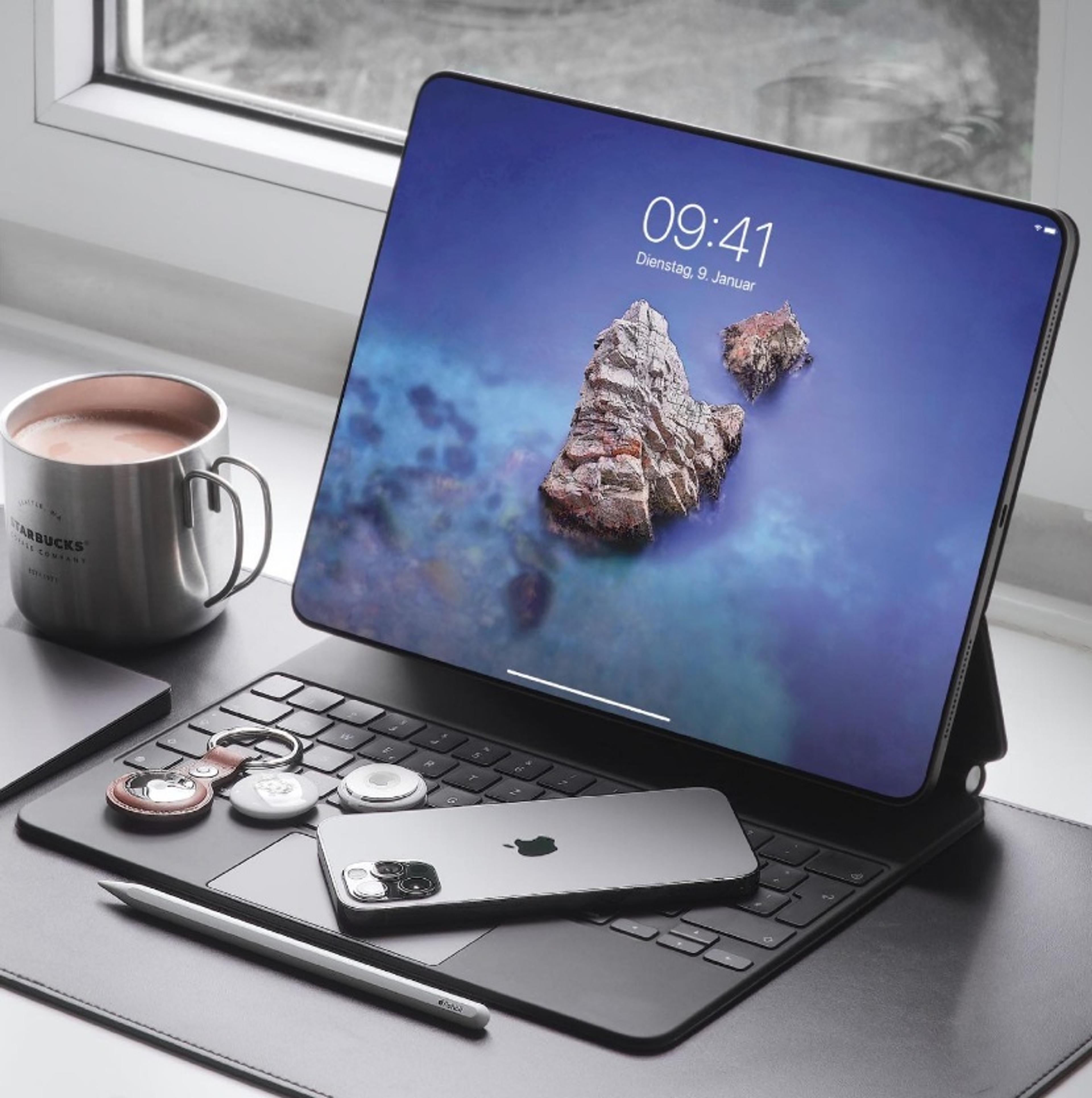 iPad with a keyboard attachment sitting open. An iPhone is laid on top of the keys and apple pencil sits in front