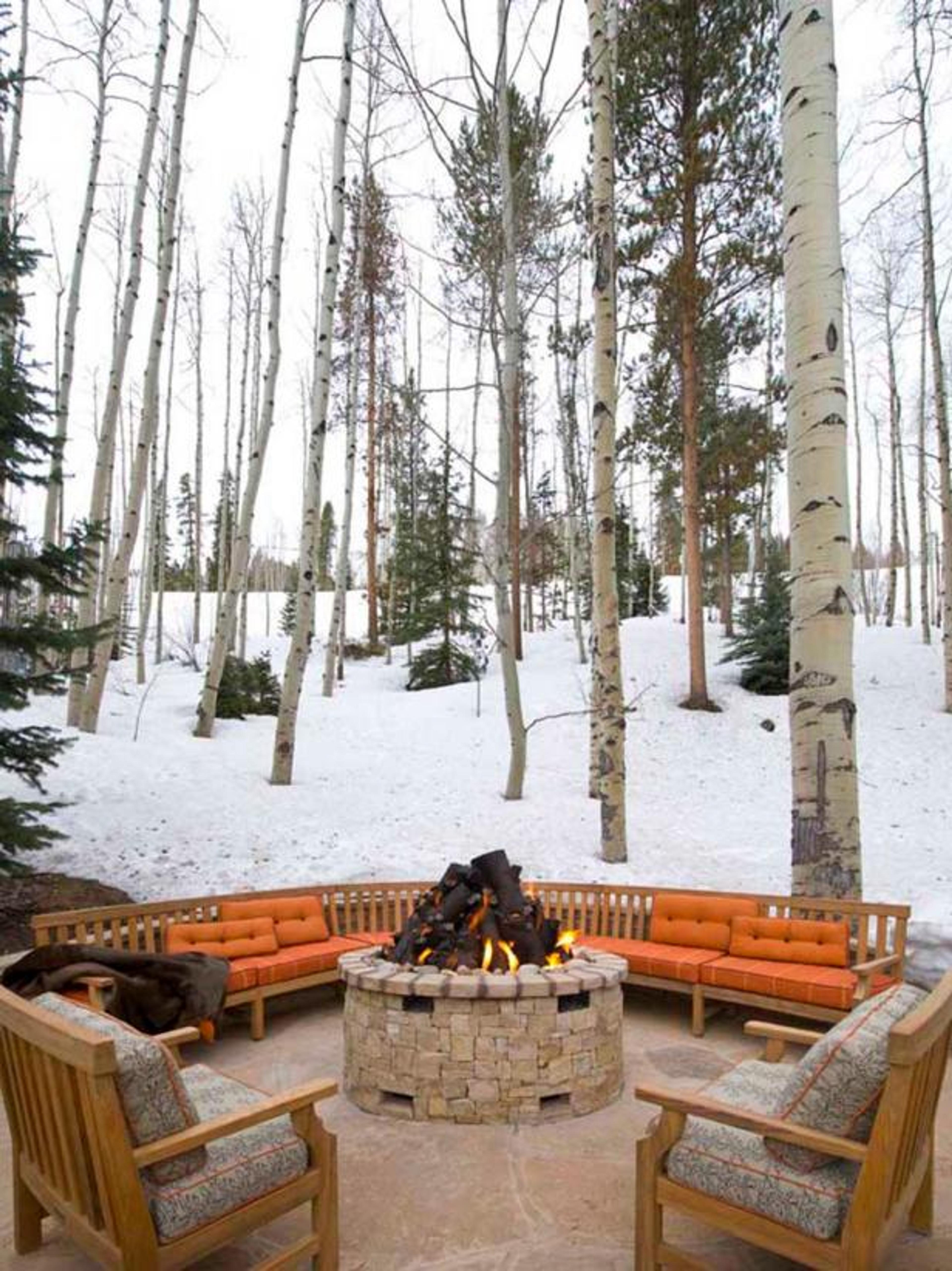 Circular patio with a large stone fire pit in the middle and lounge chairs and benches around it