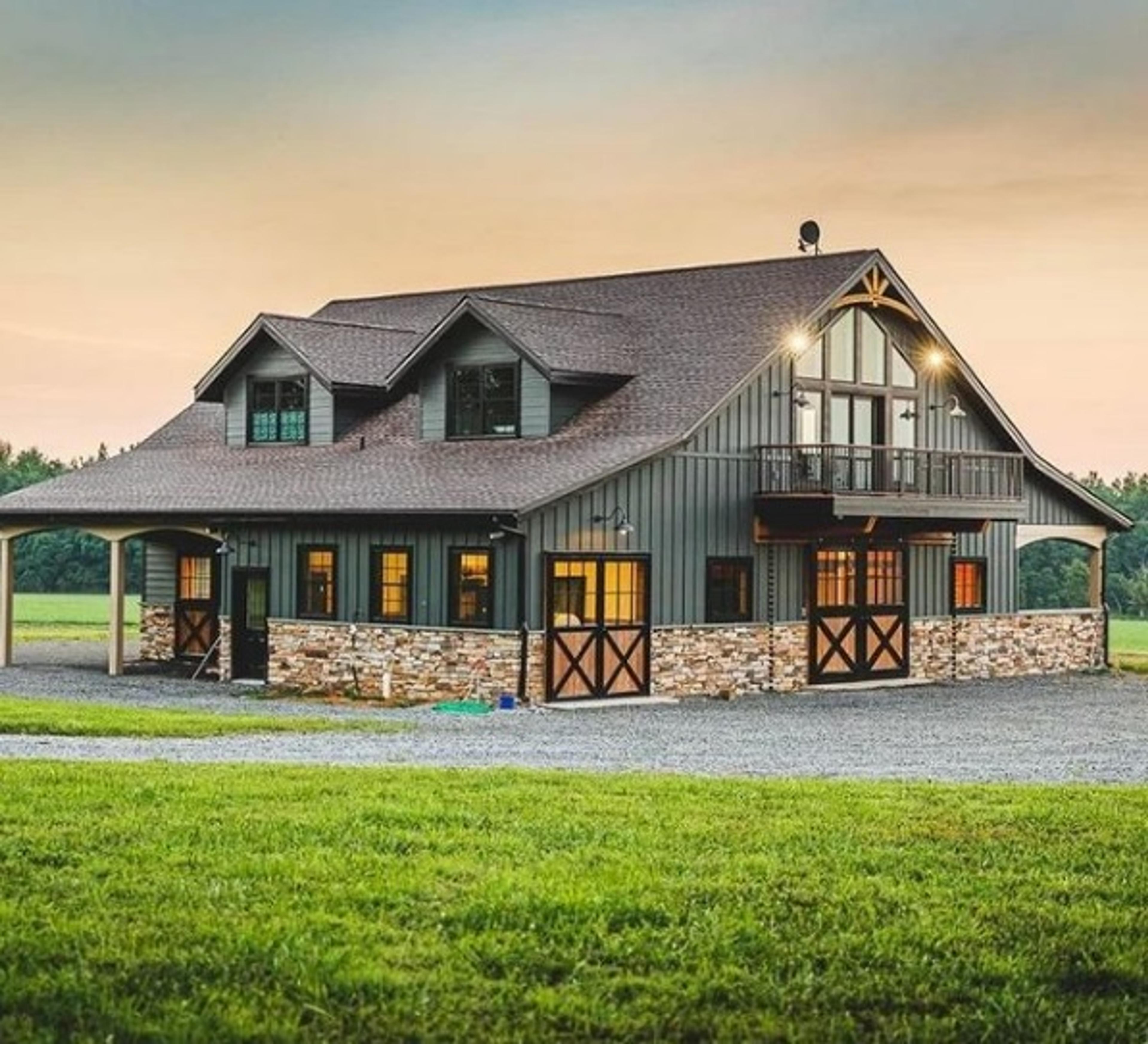 A two-story, green-sided barndominium with stone trim and a balcony