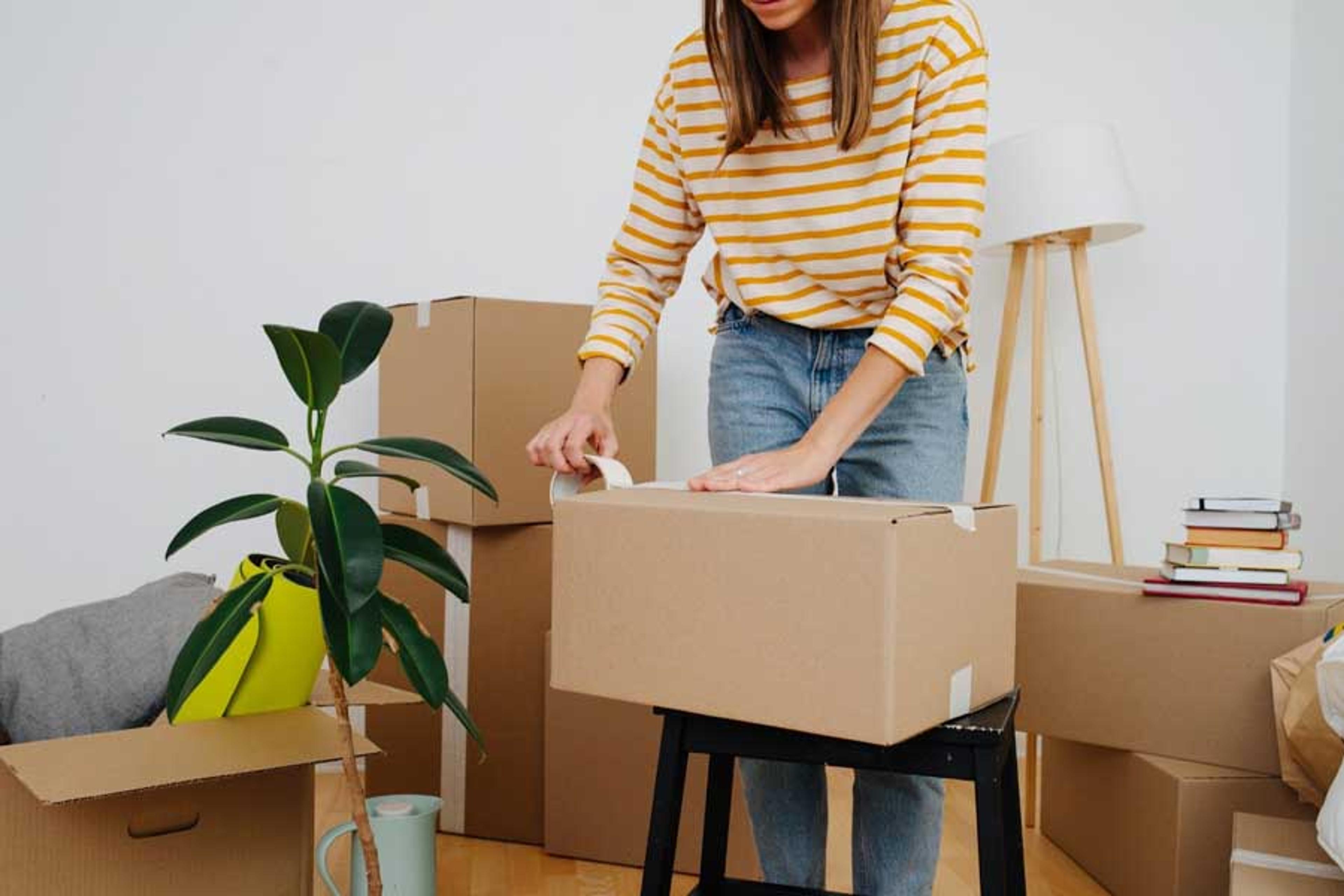Person in a packed up living room taping up a moving box