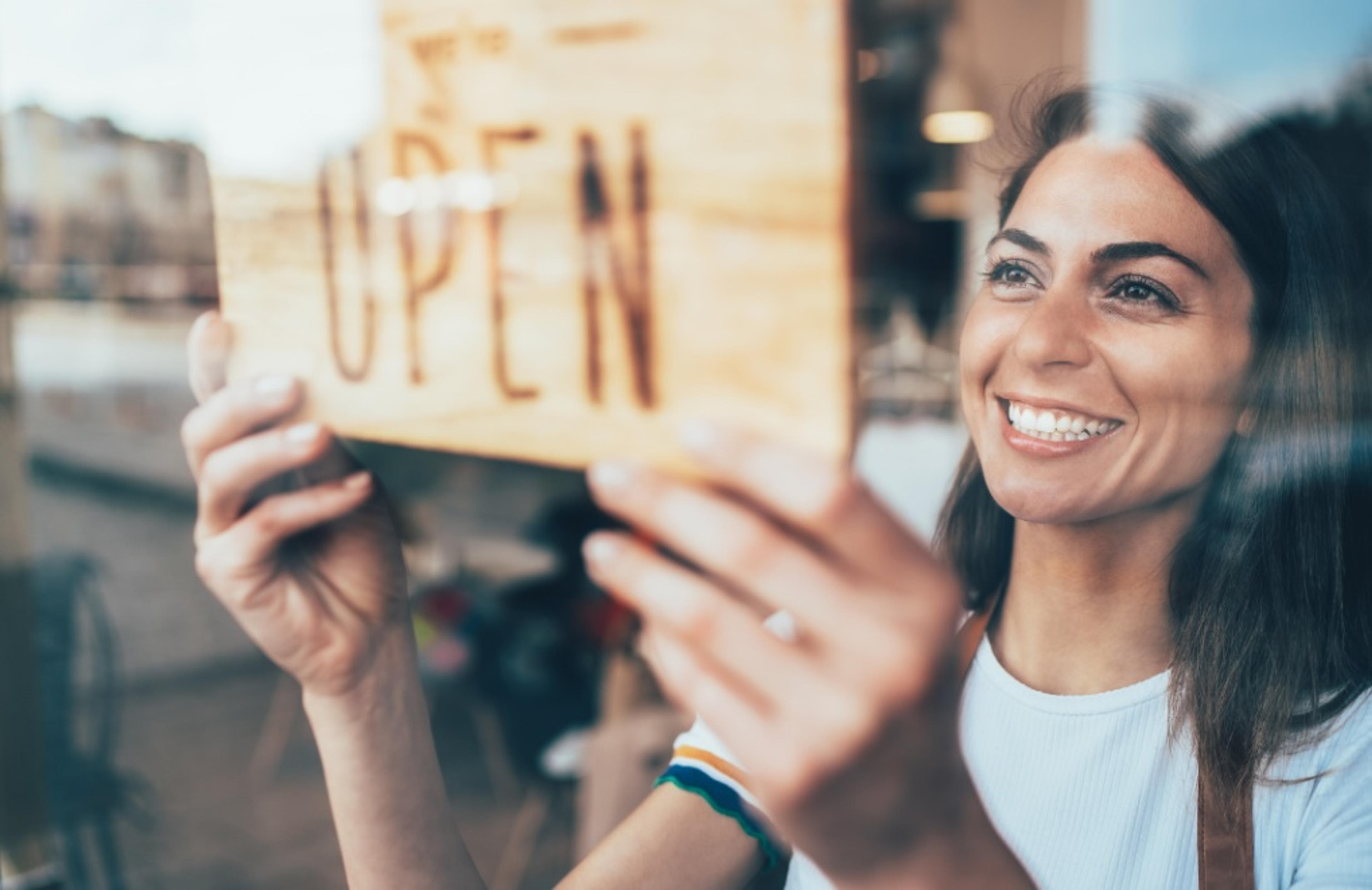 Woman smiling while flipping a shop sign to say open