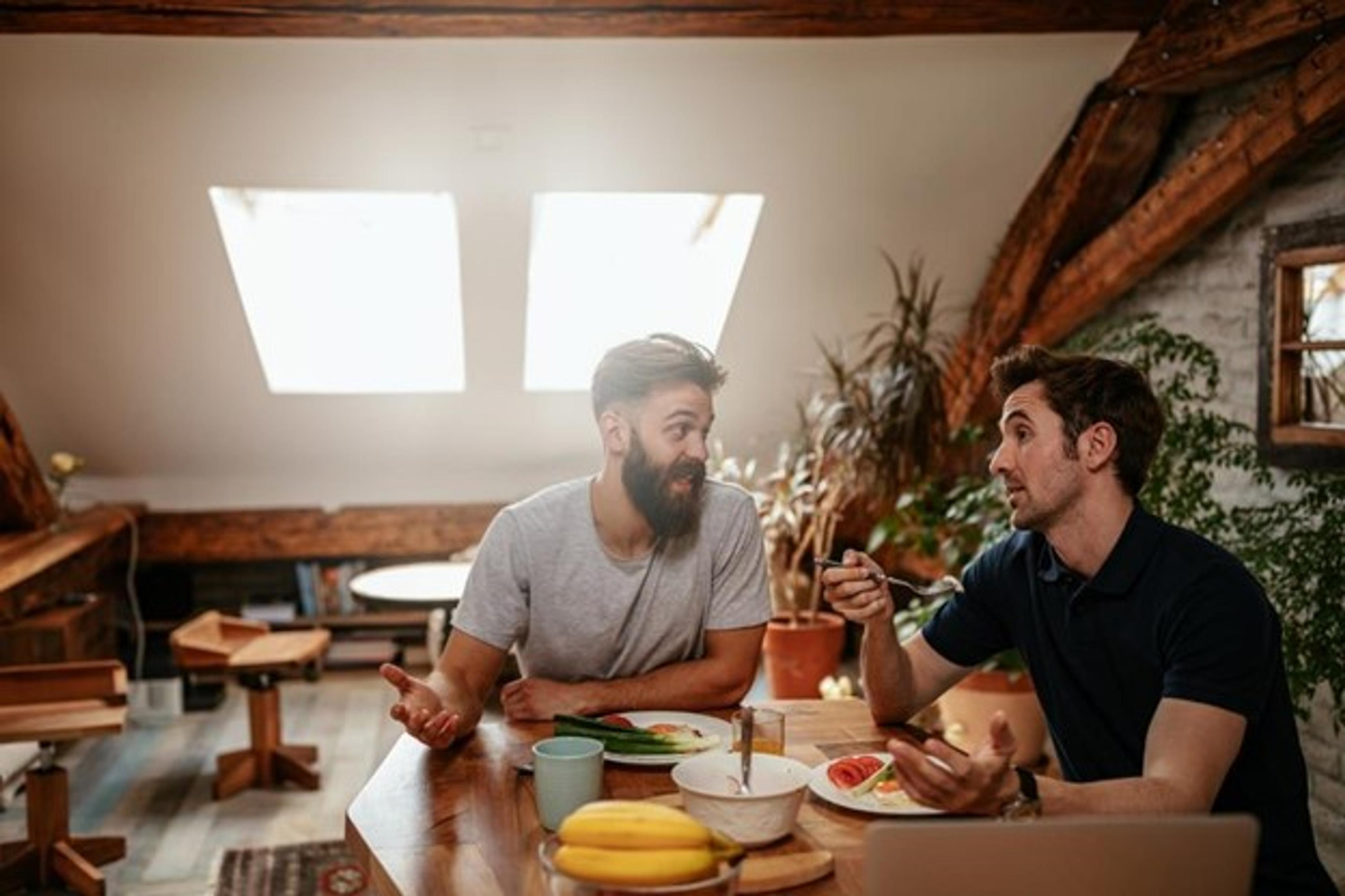 Two male roommates conversing at their apartment breakfast nook