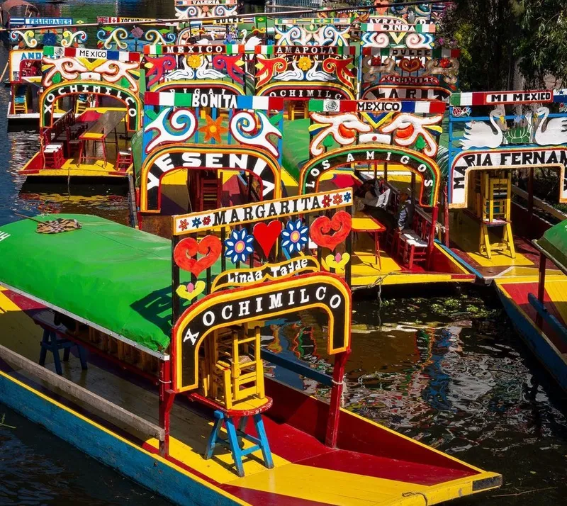 The image shows a colorful fleet of brightly painted boats called trajineras, which are traditionally used for transportation and tourism in the canals of Xochimilco, Mexico