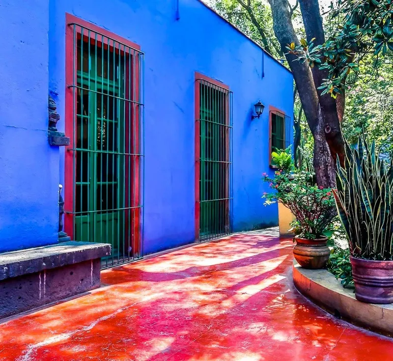 Blue building with green doors, red floor, and potted plants at Frida Kahlo Museum
