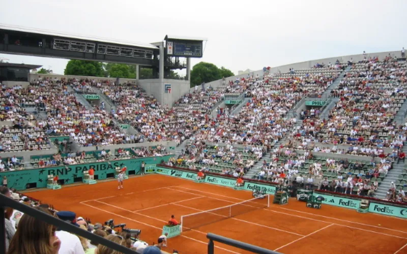A tennis court at Roland Garros Stadium with a large crowd of spectators watching the match