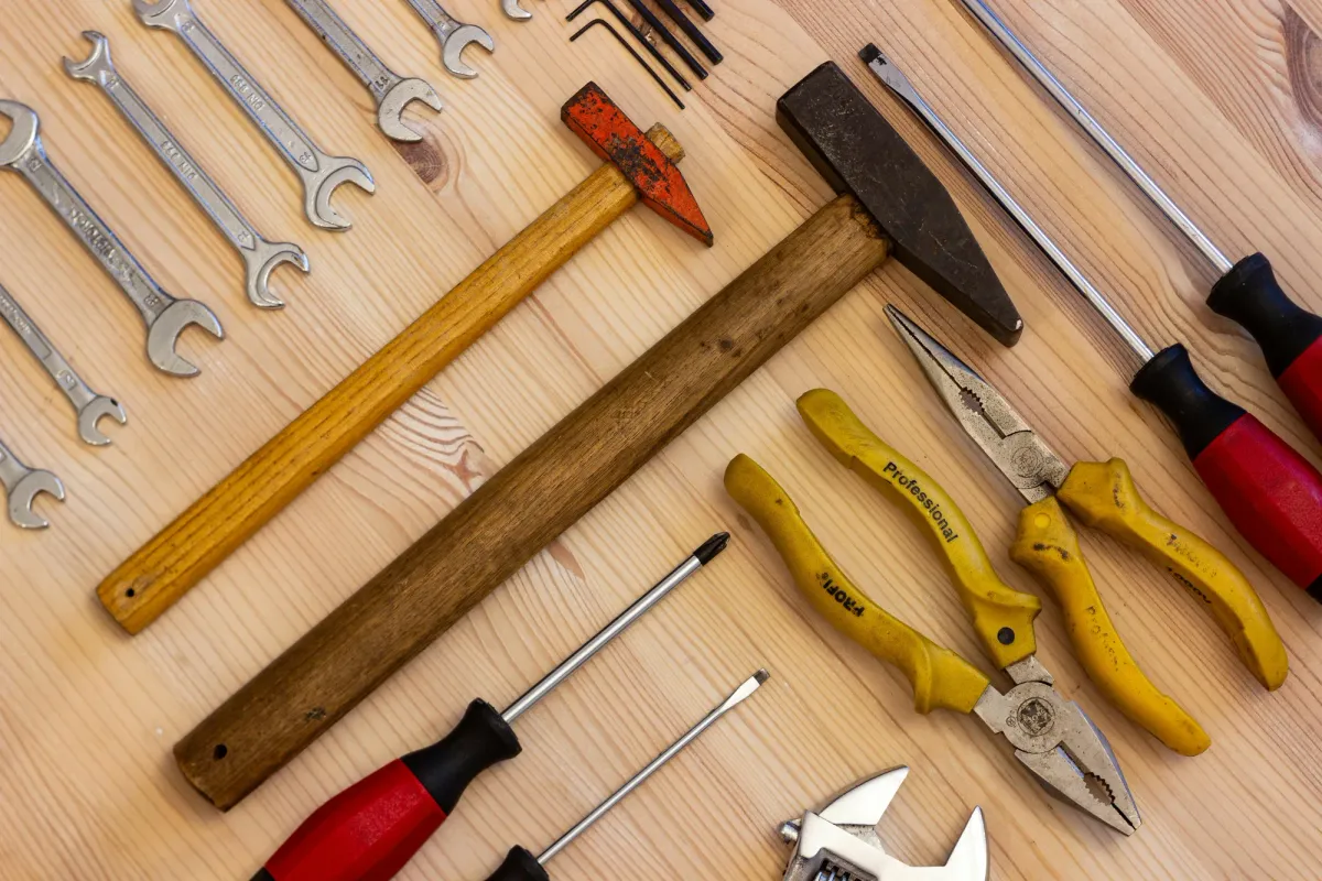 An assortment of hand tools — wrenches, a hammer, pliers, and screwdrivers — laid out on a work surface