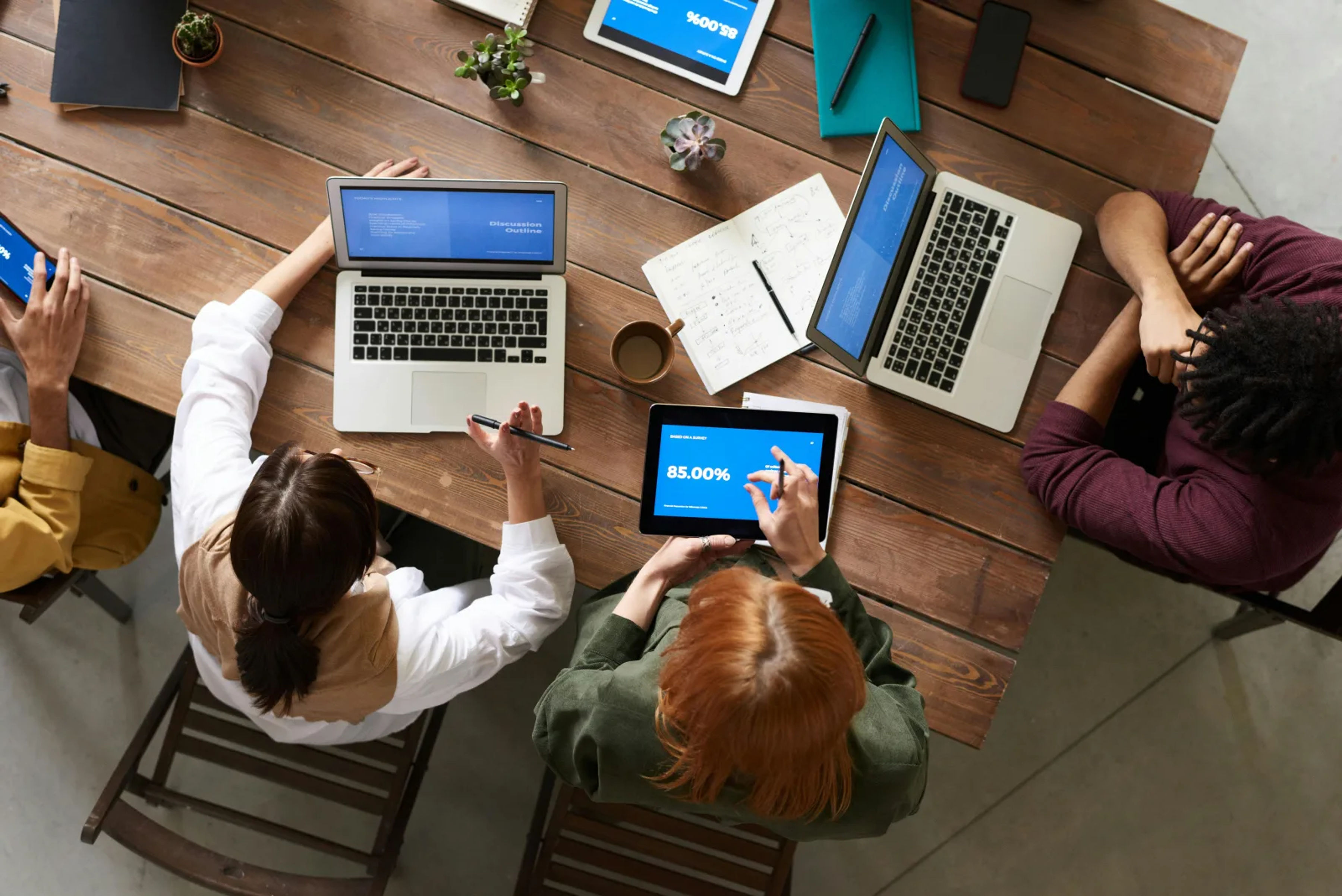 Overhead view of a facility management team collaborating around a table with laptops, documents, and coffee cups