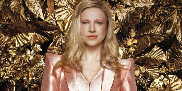 A promotional image of Hunter Schaefer as Tigris Snow in pink in front of a gold background in The Hunter Games: The Ballad of Songbirds and Snakes