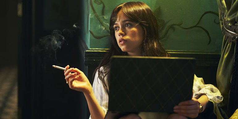 Cairo looking away with a cigarette on her hand and a lapton on her lap in Miller's Girl