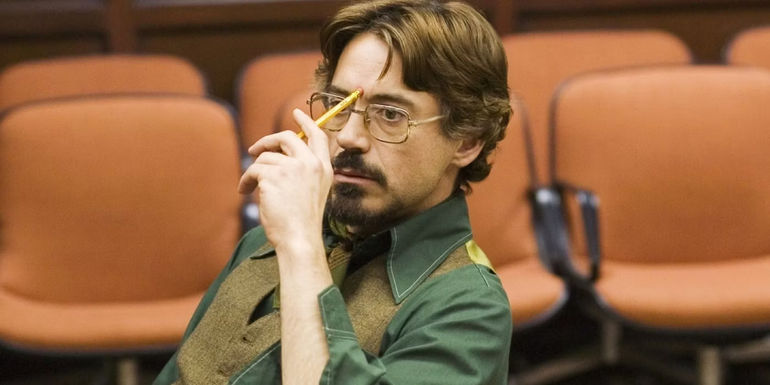 Robert Downey Jr sitting and holding a pencil to his head in Zodiac