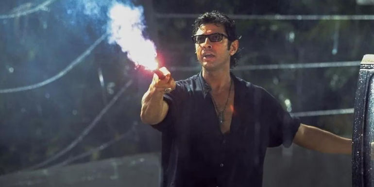 Jeff Goldblum's Ian Malcolm holding a flare beside a broken fence in Jurassic Park