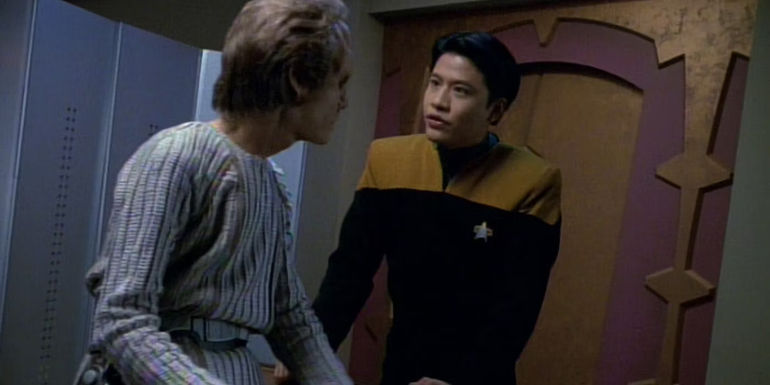 harry kim leans over to confront a sitting alien man in voyager emanations