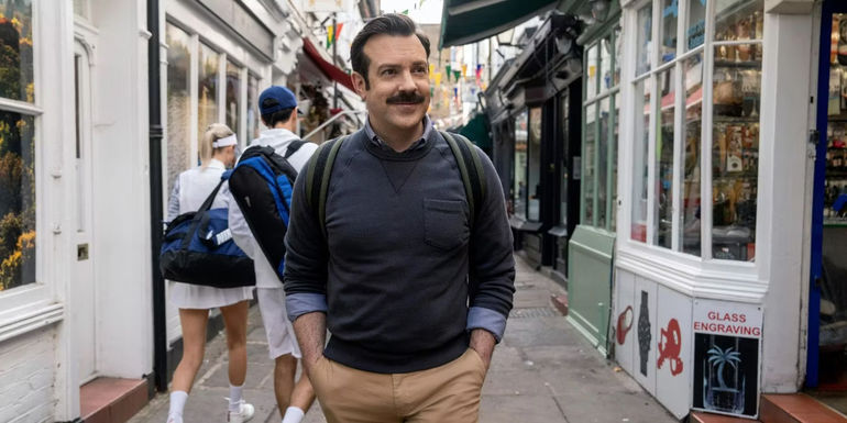 Ted (Jason Sudeikis) smiling and walking down the street in Ted Lasso season 3 episode 11 Mom City.