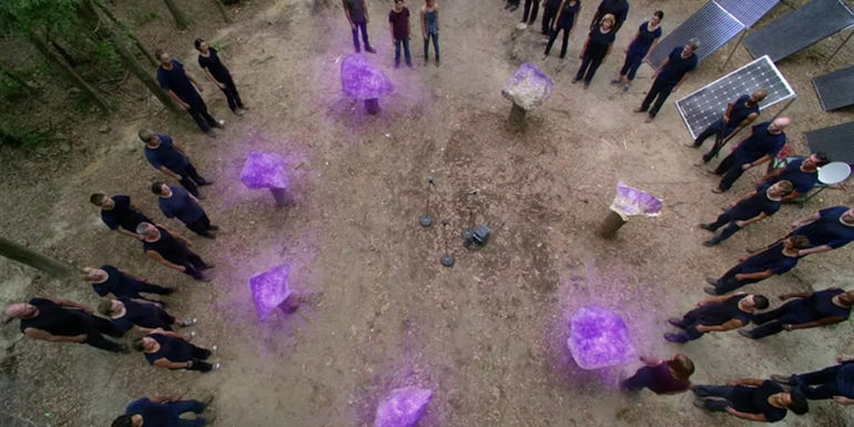 Rocks in a circle being activated and emitting a purple glow as people watch in Under the Dome.