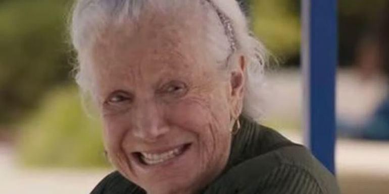 An older woman smiling on a bench in Barbie