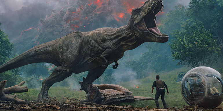 A T-rex roars beside a volcano as Chris Pratt's Owen stands by a gyrosphere in Jurassic World Fallen Kingdom
