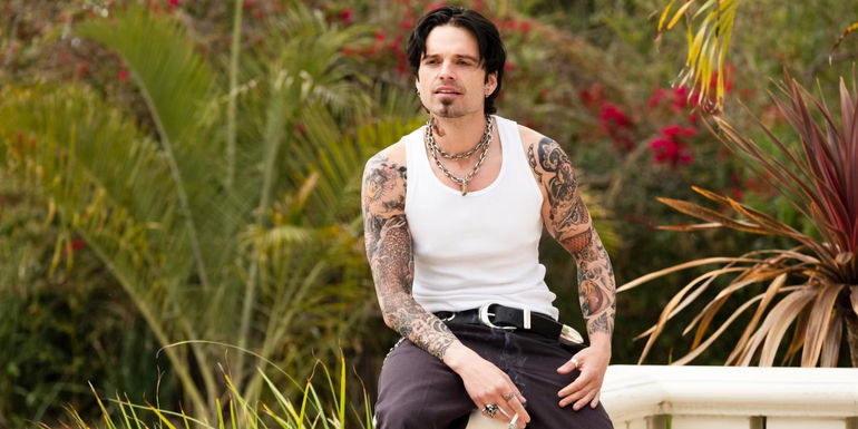Sebastian Stan's Tommy Lee sitting on ledge with cigarette in hand in Pam and Tommy