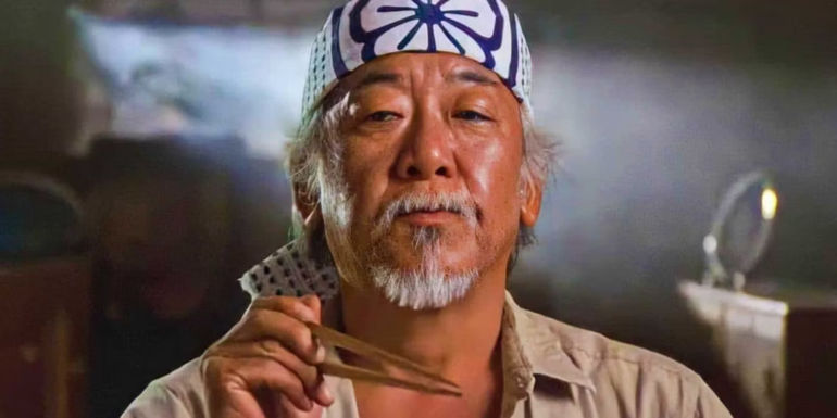 Pat Morita holding chopsticks as Mr. Miyagi in The Karate Kid