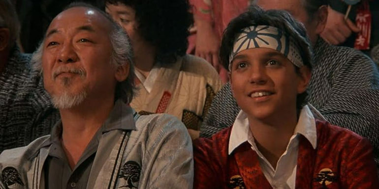Pat Morita as Mr. Miyagi and Ralph Macchio as Daniel LaRusso smiling in The Karate Kid