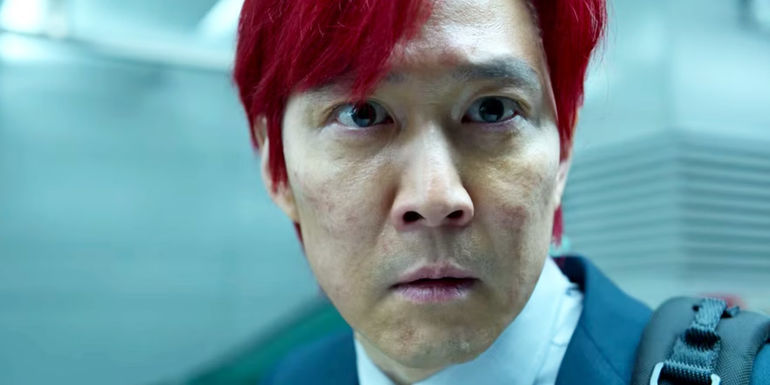 Gi-hun wears red hair and a suit while looking alarmed in Squid Game.