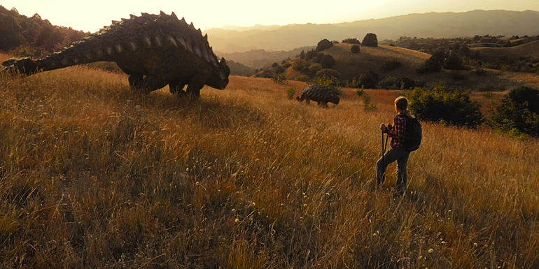 A hiker looks at a passing dinosaur in Jurassic World Dominion