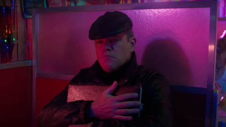 Matt Damon clutching a briefcase to his chest in Drive-Away Dolls