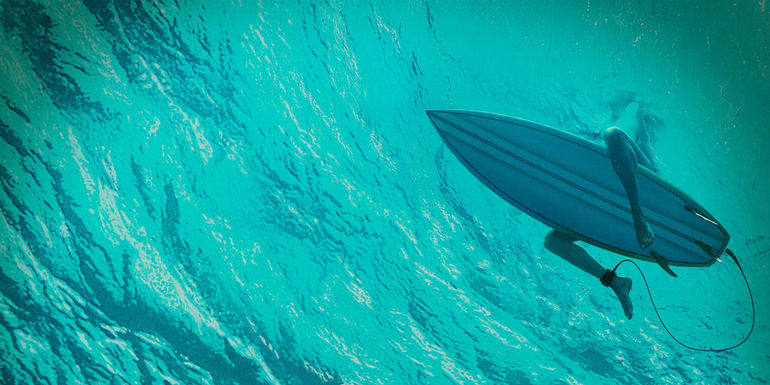 A shot from underwater of a surfer sitting on a board in The Shallows