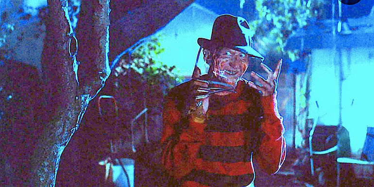 Freddy Krueger (Robert Englund) stands beside a tree grinning in Nightmare On Elm Street
