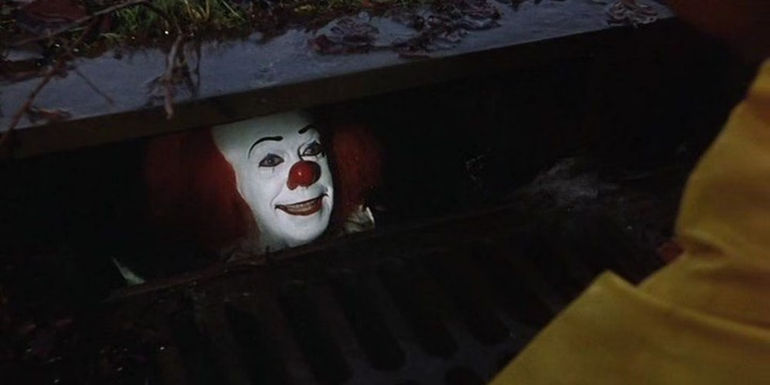 Pennywise smiles at Georgie from down the storm drain in the IT miniseries.