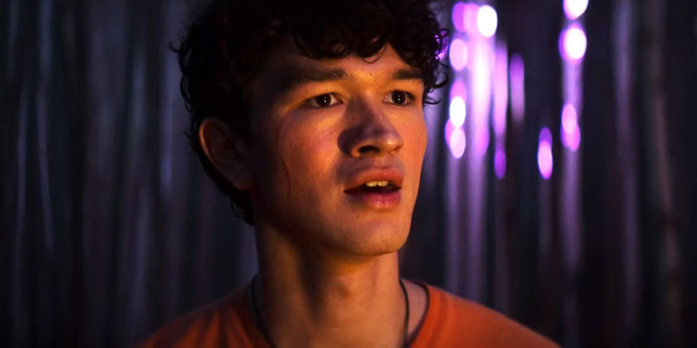 Luke in the woods with purple lighting in the distance in Percy Jackson episode 8