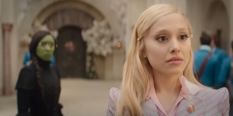 An out-of-focus Elphaba (Cynthia Erivo) stands behind Glinda (Ariana Grande) in Wicked.