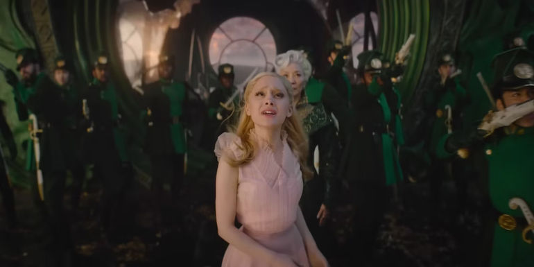 Glinda (Ariana Grande) looks up with guards and Madame Morrible standing behind her in Wicked.
