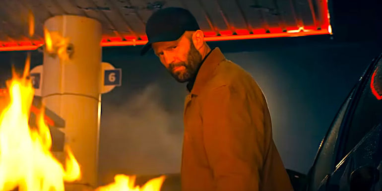 Jason Statham looks satisfied with himself while flames burn all around in an action scene fromThe Beekeeper-1